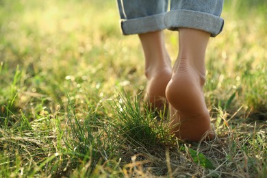 Photo of Woman walking barefoot on green grass outdoors, closeup. Space for text