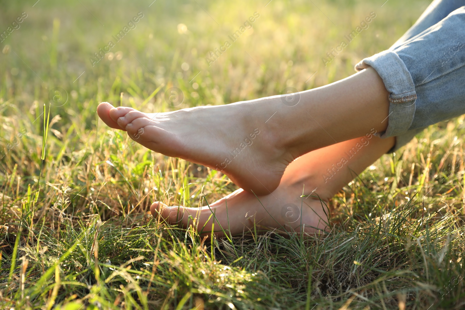 Photo of Woman sitting barefoot on green grass outdoors, closeup