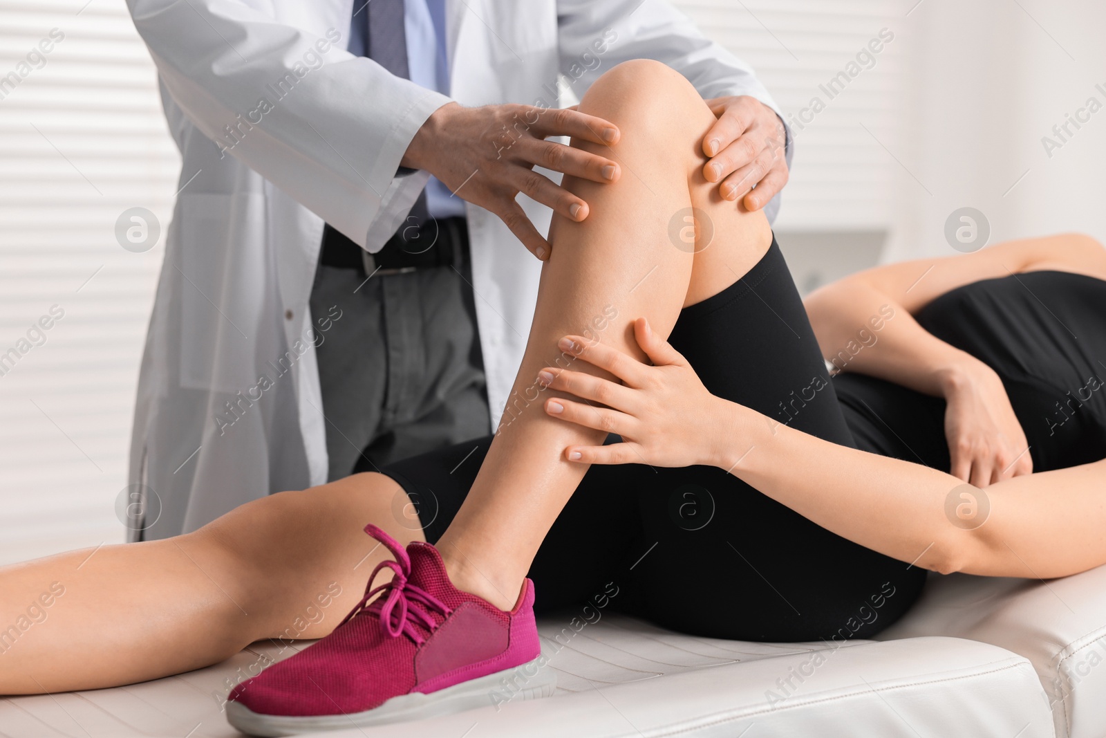 Photo of Sports injury. Doctor examining patient's knee in hospital, closeup