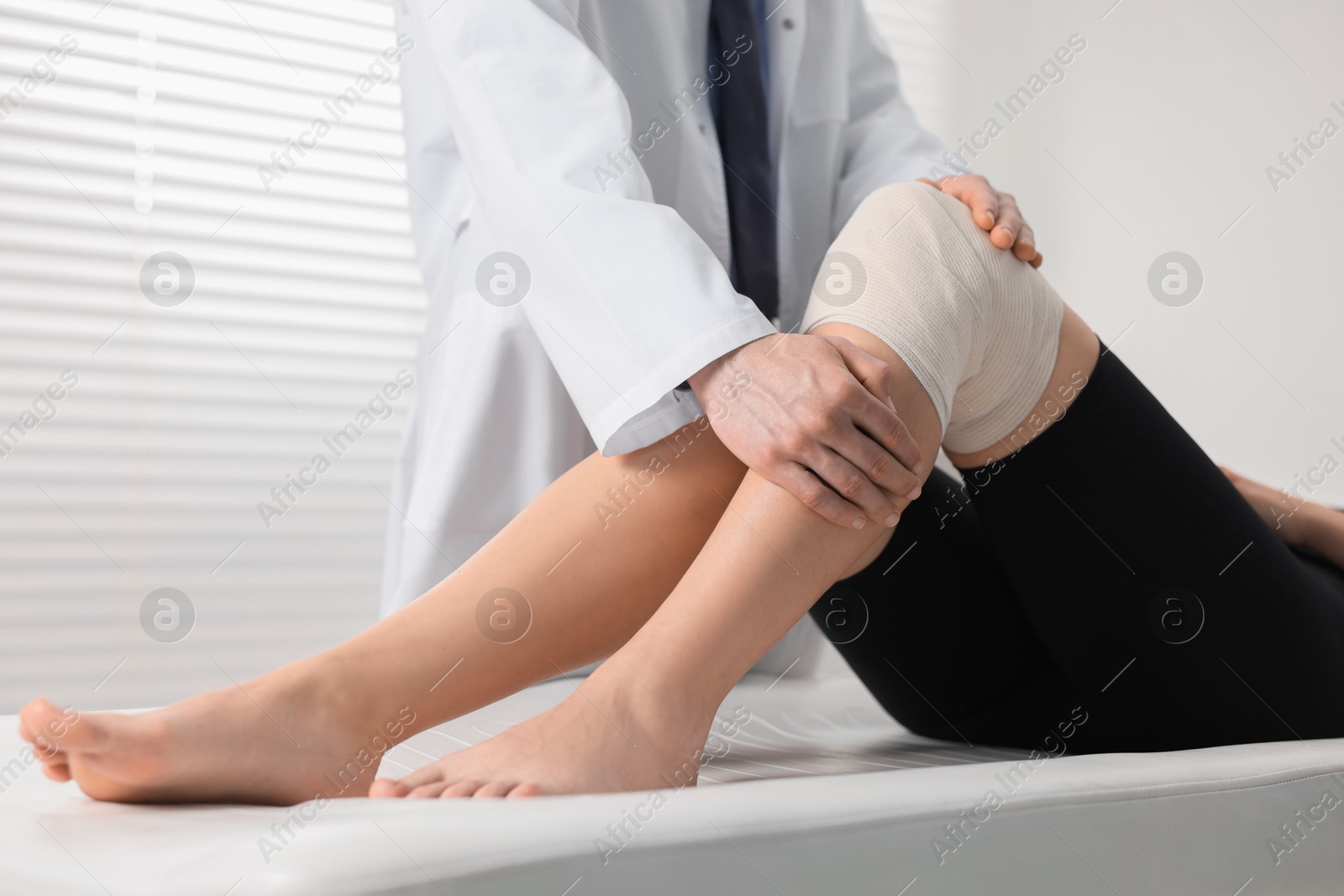 Photo of Sports injury. Doctor examining patient's knee in hospital, closeup