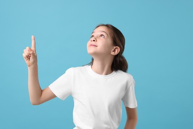 Beautiful girl pointing at something on light blue background