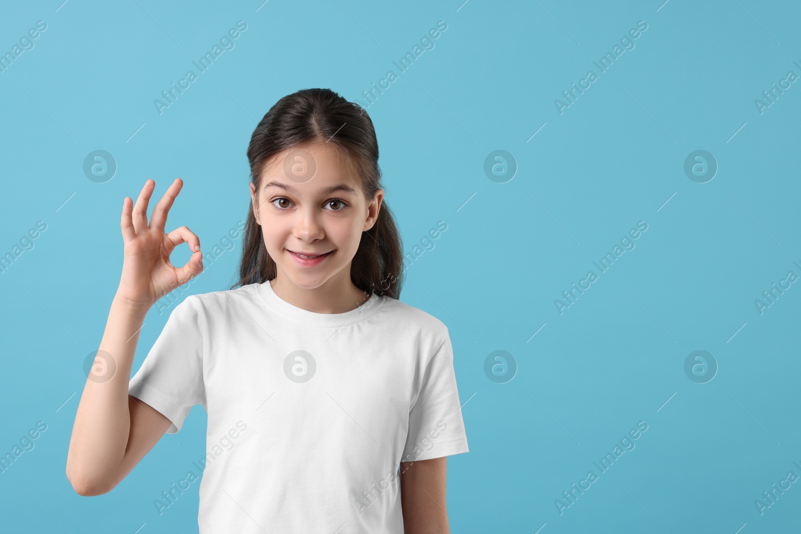 Photo of Portrait of beautiful girl showing Ok gesture on light blue background, space for text