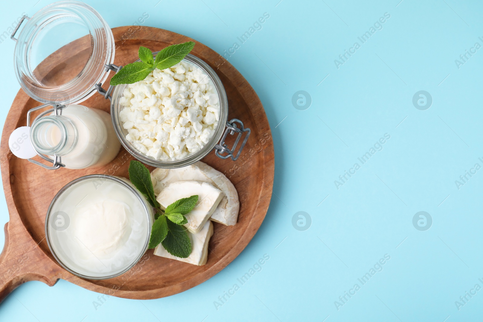 Photo of Different dairy products and mint on light blue background, top view. Space for text