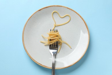Photo of Heart made of tasty spaghetti and fork on light blue background, top view