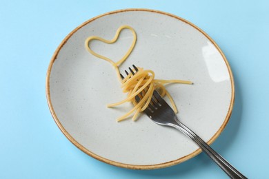 Photo of Heart made of tasty spaghetti and fork on light blue background