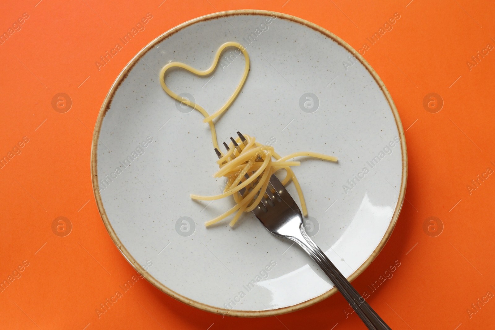 Photo of Heart made of tasty spaghetti and fork on orange background, top view