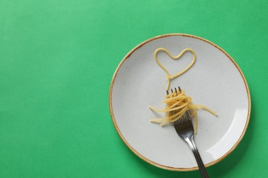 Photo of Heart made of tasty spaghetti and fork on green background, top view. Space for text