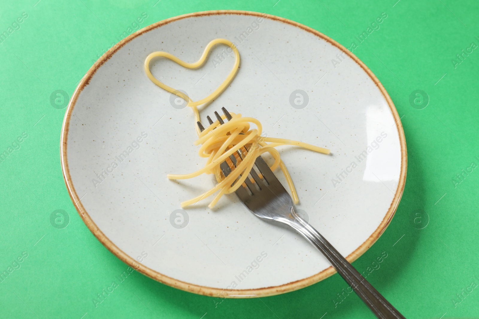 Photo of Heart made of tasty spaghetti and fork on green background