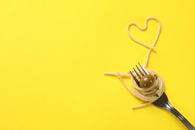 Photo of Heart made of tasty spaghetti, fork and olive on yellow background, top view. Space for text