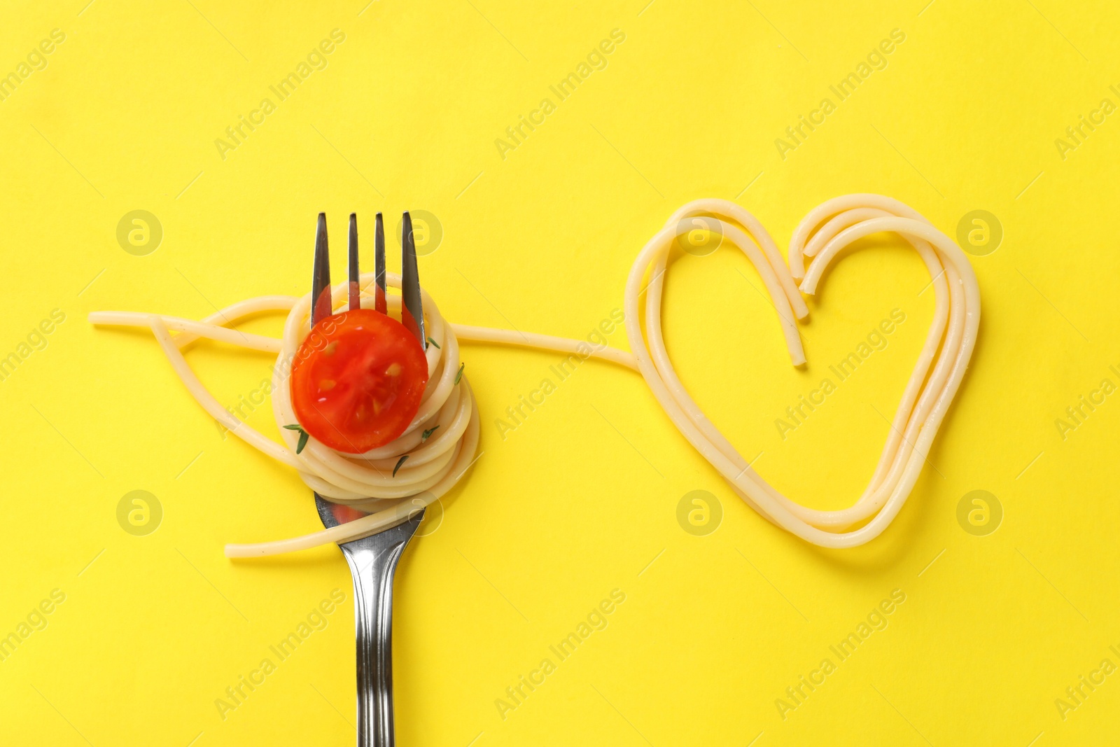 Photo of Heart made of tasty spaghetti, fork and tomato on yellow background, top view