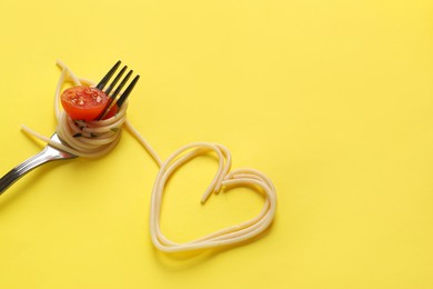 Heart made of tasty spaghetti, fork and tomato on yellow background. Space for text