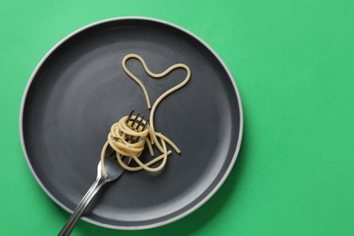 Photo of Heart made of tasty spaghetti and fork on green background, top view. Space for text