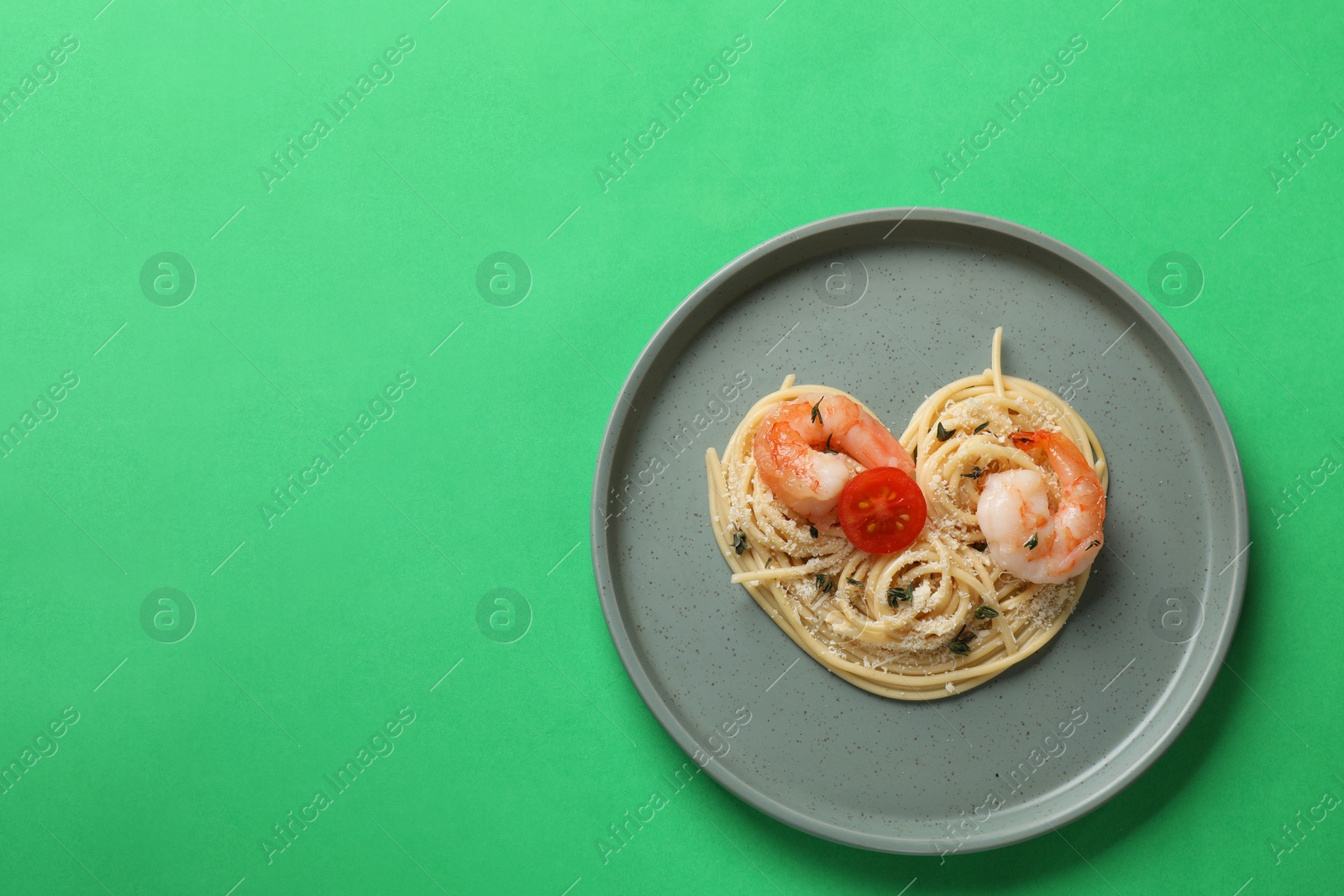 Photo of Heart made of tasty spaghetti, tomato, shrimps and cheese on green background, top view. Space for text