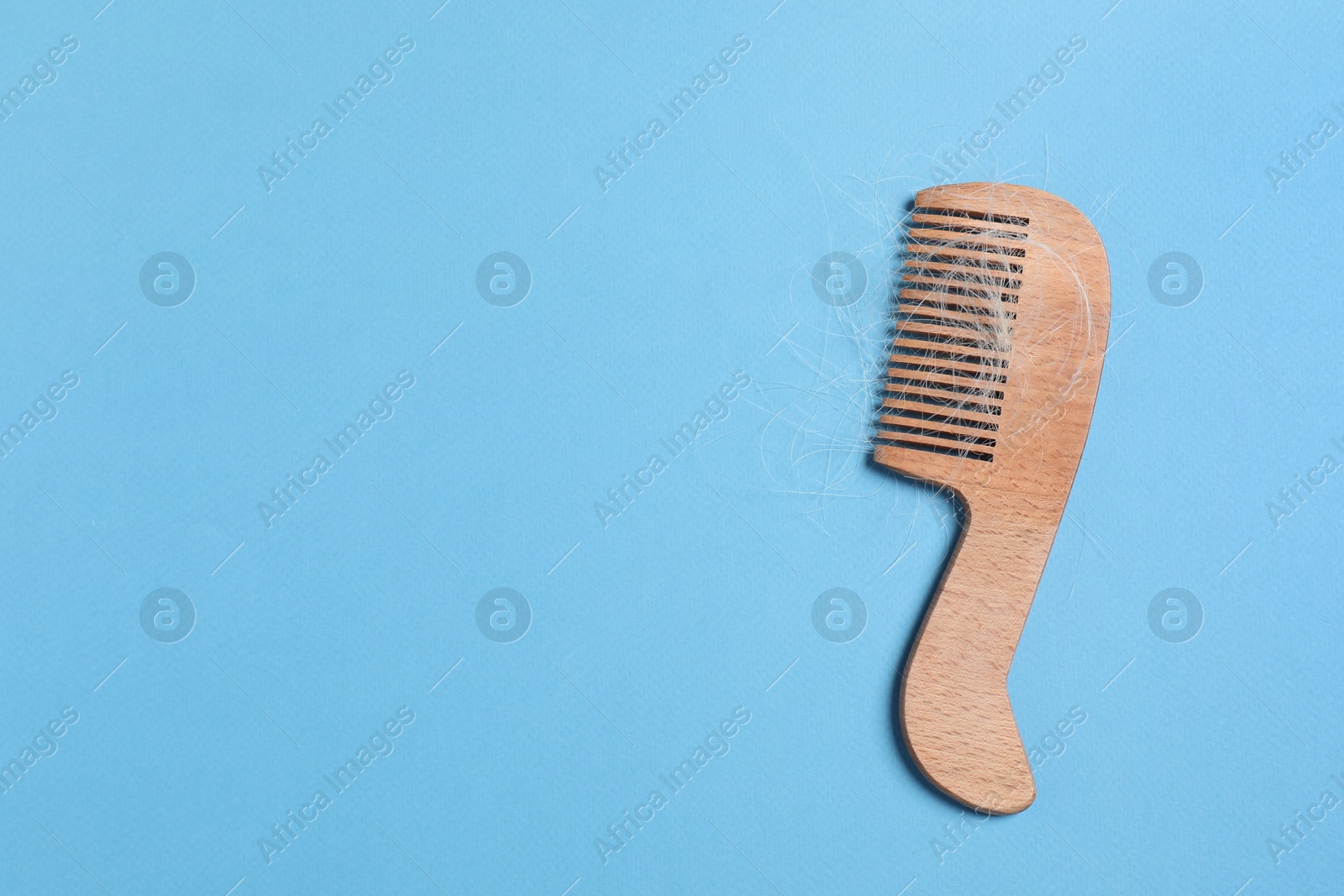 Photo of Wooden comb with lost hair on light blue background, top view. Space for text