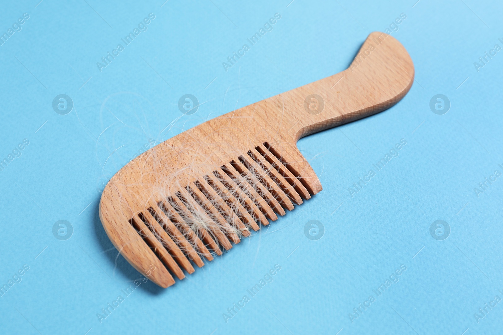 Photo of Wooden comb with lost hair on light blue background