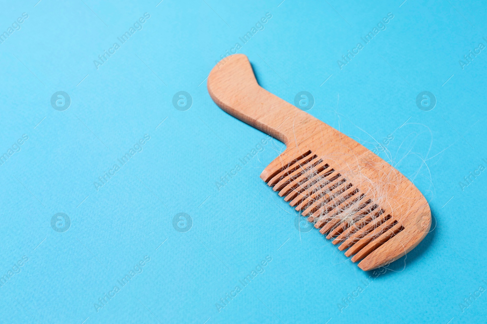 Photo of Wooden comb with lost hair on light blue background, space for text