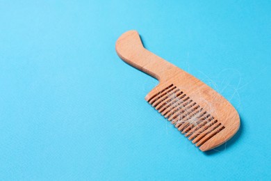 Photo of Wooden comb with lost hair on light blue background, space for text