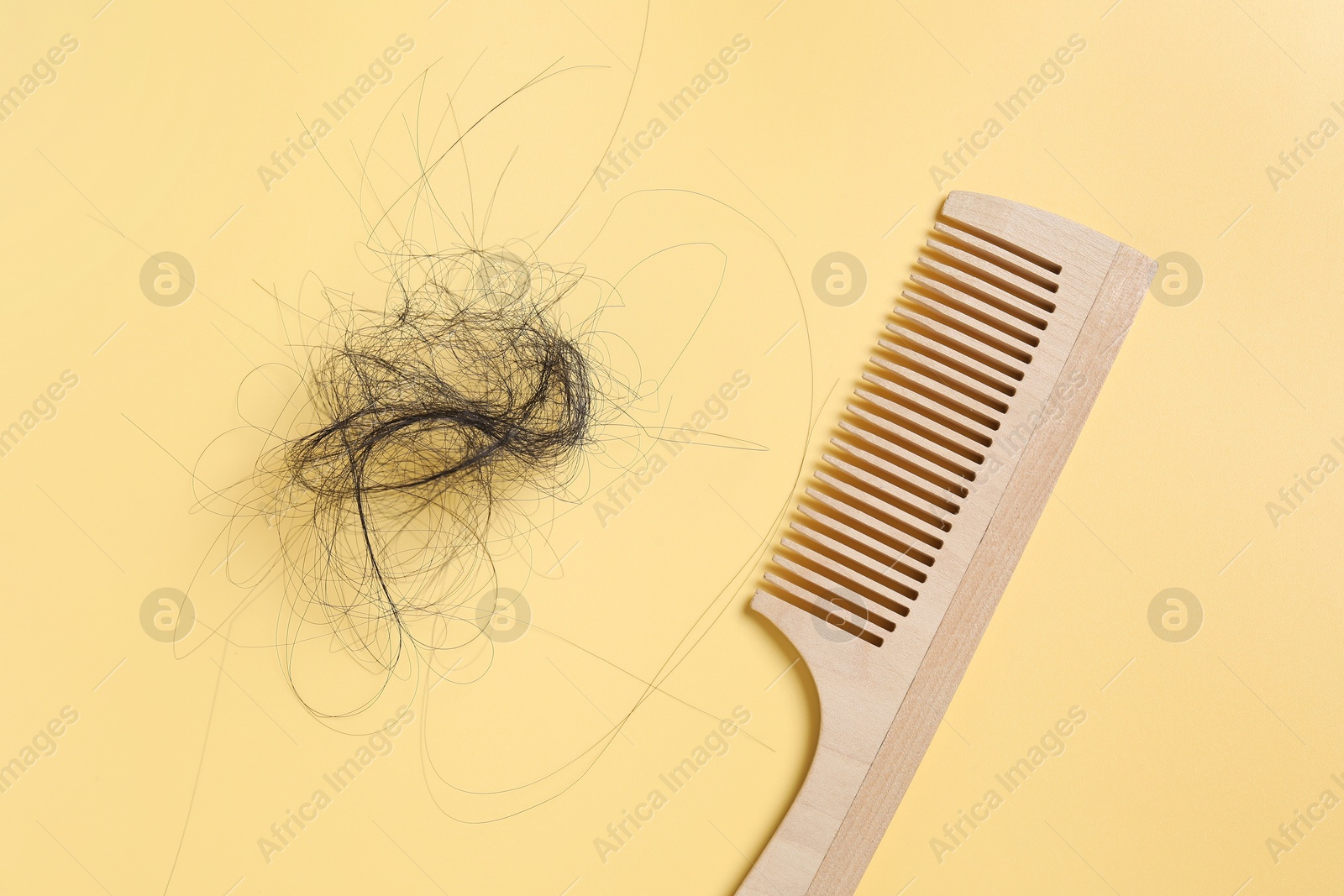 Photo of Wooden comb with lost hair on yellow background, top view