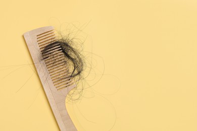 Photo of Wooden comb with lost hair on yellow background, top view. Space for text