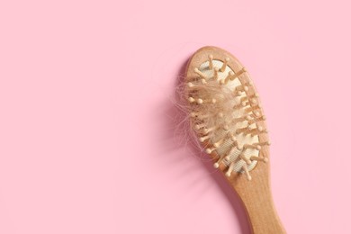 Photo of Wooden brush with lost hair on pink background, top view. Space for text