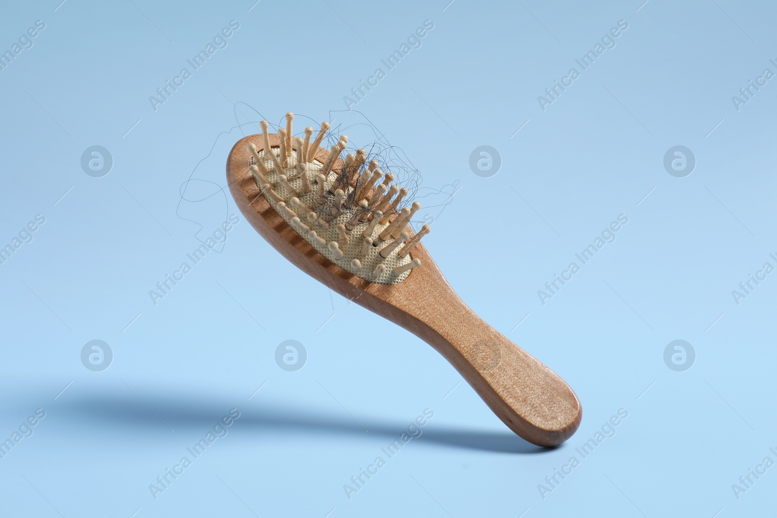 Photo of Wooden brush with lost hair in air on light blue background