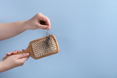 Photo of Woman taking her lost hair from brush on light blue background, closeup. Space for text