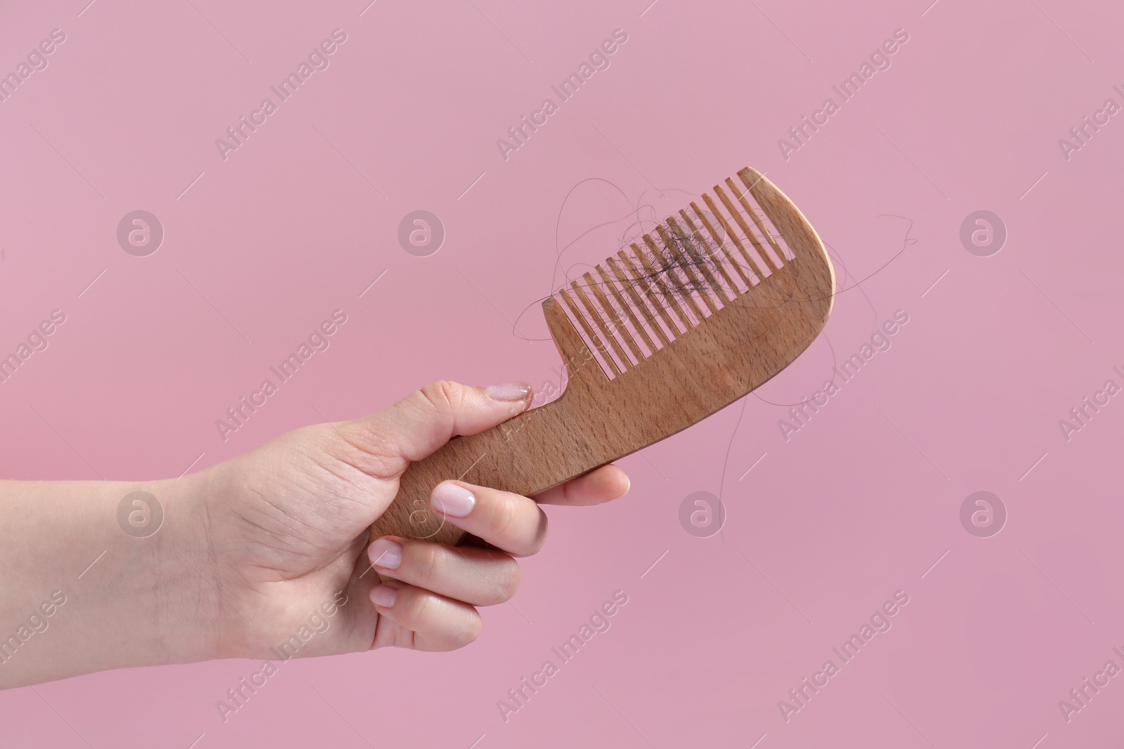 Photo of Woman holding comb with lost hair on pink background, closeup