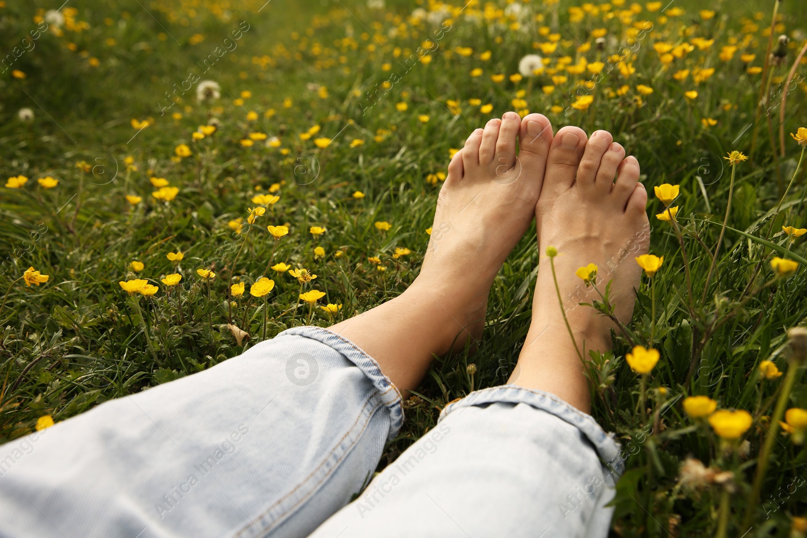 Photo of Woman sitting barefoot on green grass outdoors, closeup