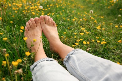 Photo of Woman sitting barefoot on green grass outdoors, closeup