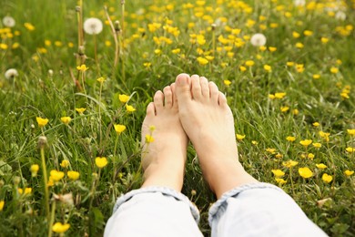 Photo of Woman sitting barefoot on green grass outdoors, closeup