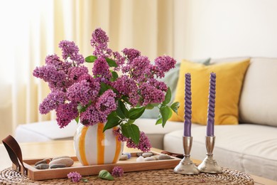 Photo of Beautiful lilac flowers in vase and candles on table at home