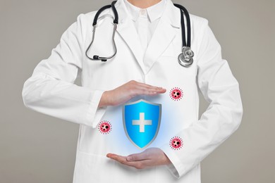 Strong immunity blocking viruses. Doctor holding illustration of shield on grey background, closeup