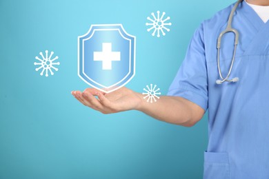 Image of Strong immunity blocking viruses. Doctor holding illustration of shield on light blue background, closeup