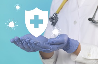 Strong immunity blocking viruses. Doctor holding illustration of shield on light blue background, closeup