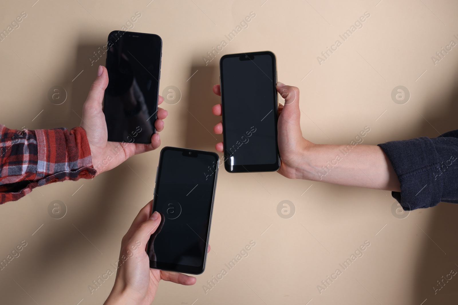 Photo of Women holding smartphones with blank screens against beige background, closeup. Mockup for design