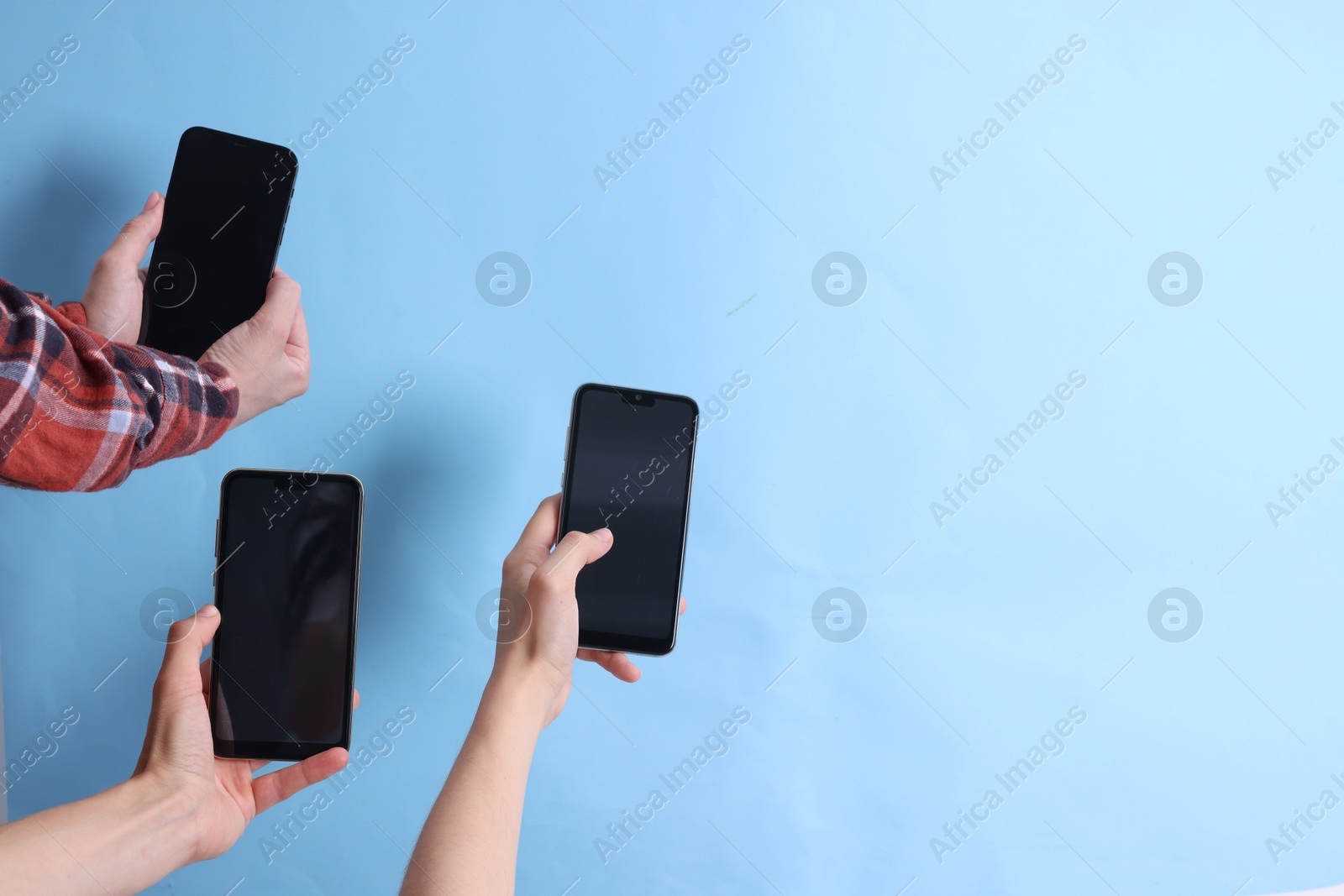 Photo of Women holding smartphones with blank screens against light blue background, closeup. Mockup for design