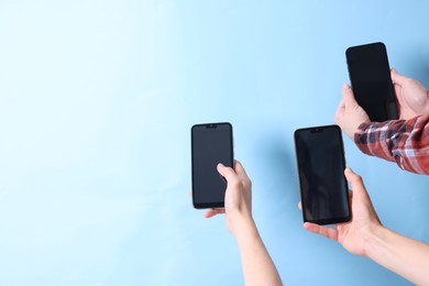 Photo of Women holding smartphones with blank screens against light blue background, closeup. Mockup for design