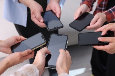 Photo of People holding smartphones with blank screens indoors, closeup