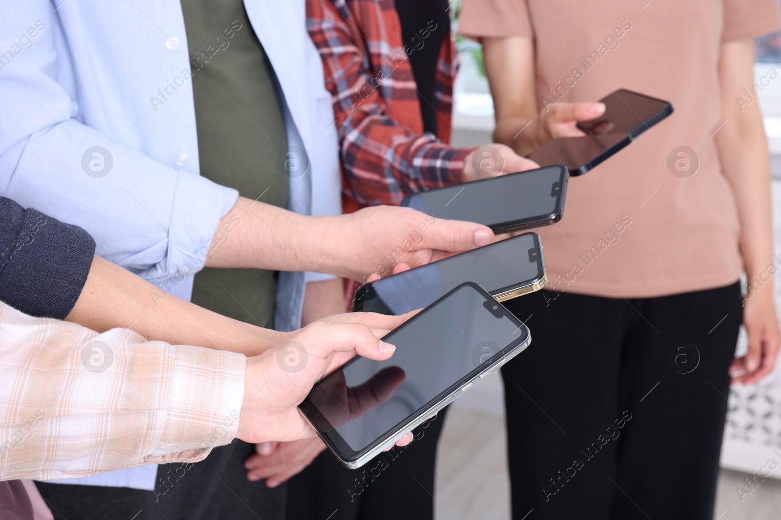 Photo of People holding smartphones with blank screens indoors, closeup