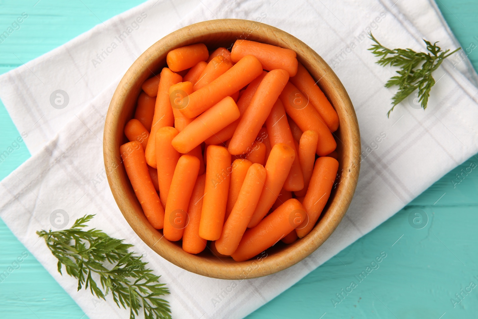 Photo of Baby carrots and green leaves on light blue wooden table, top view