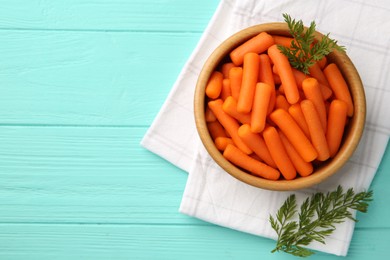 Baby carrots and green leaves on light blue wooden table, top view. Space for text