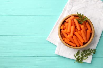 Baby carrots and green leaves on light blue wooden table, top view. Space for text