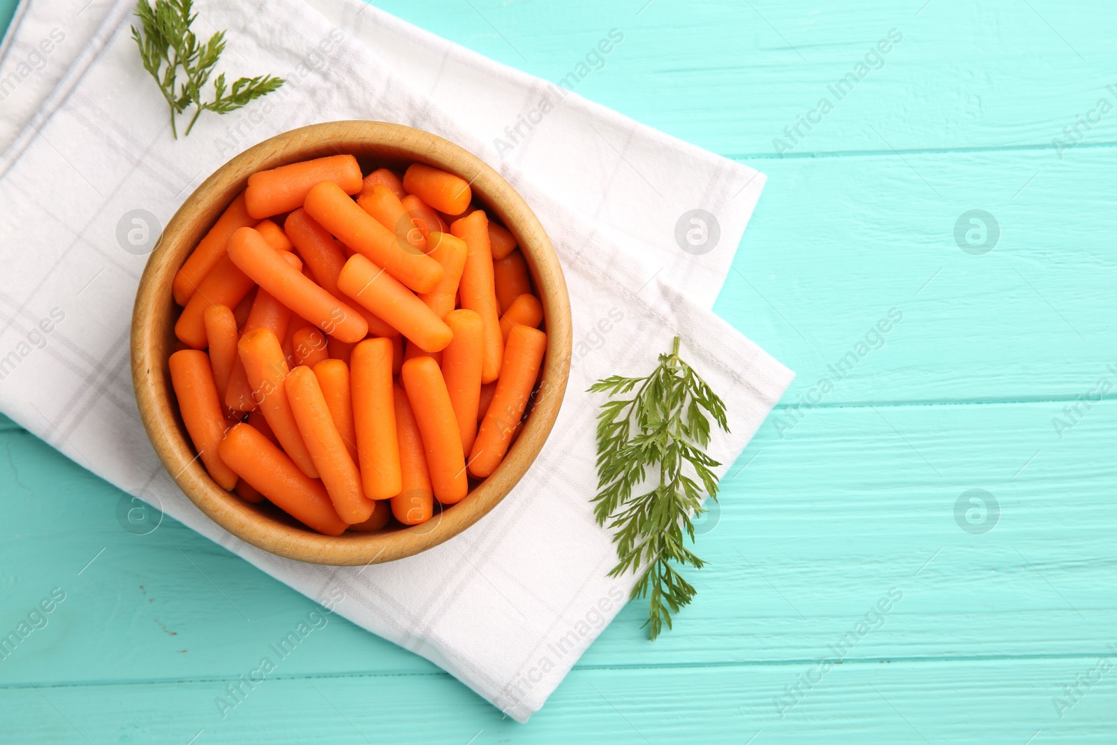 Photo of Baby carrots and green leaves on light blue wooden table, top view. Space for text