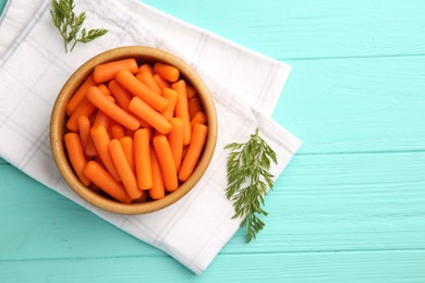 Baby carrots and green leaves on light blue wooden table, top view. Space for text