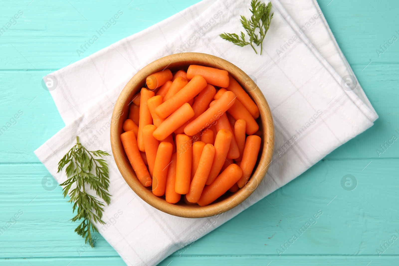 Photo of Baby carrots and green leaves on light blue wooden table, top view