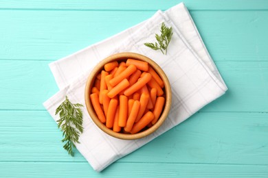 Baby carrots and green leaves on light blue wooden table, top view