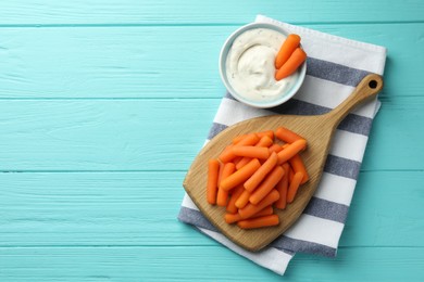 Photo of Baby carrots and sauce on light blue wooden table, top view. Space for text