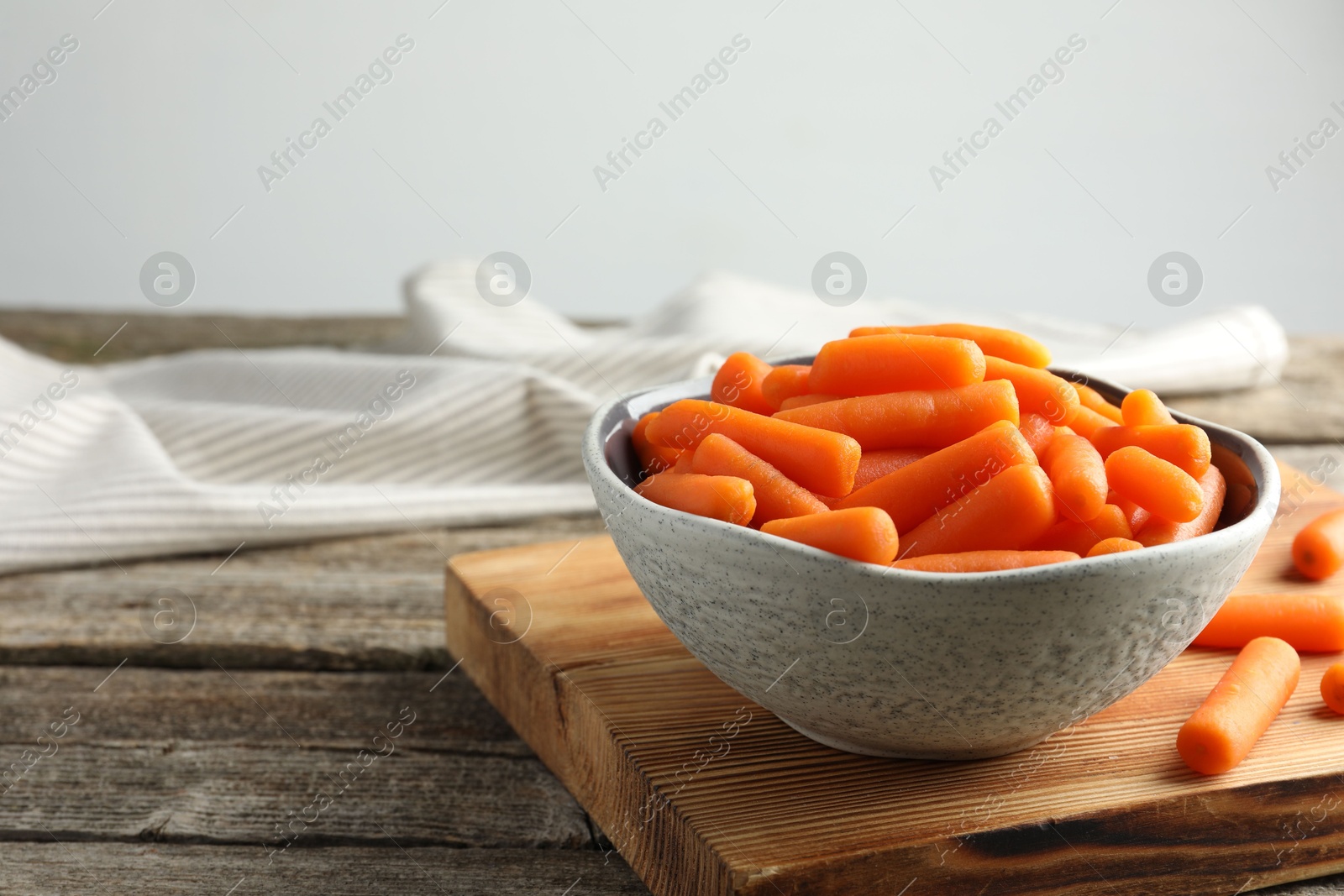 Photo of Baby carrots in bowl on wooden table, space for text