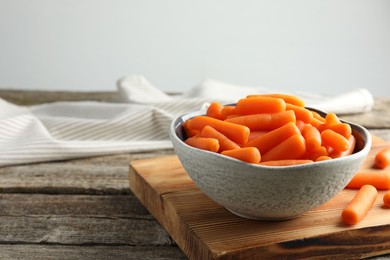 Photo of Baby carrots in bowl on wooden table, space for text