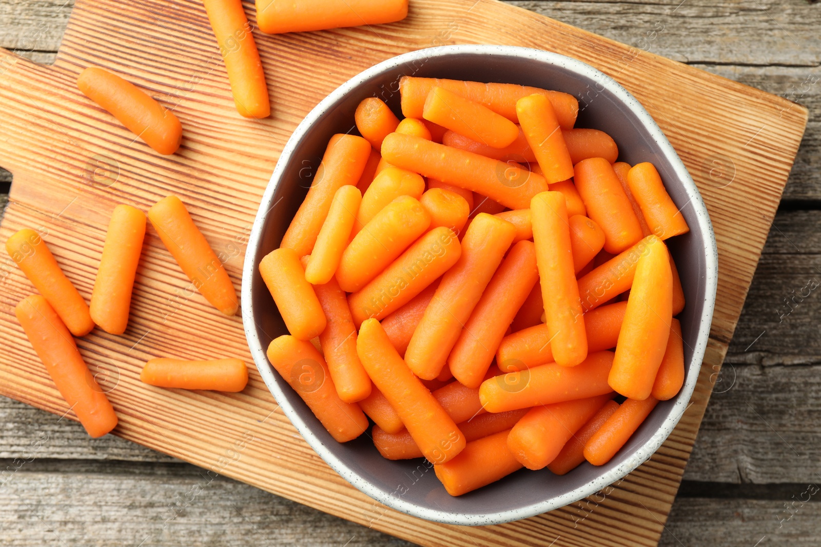 Photo of Baby carrots in bowl on wooden table, top view